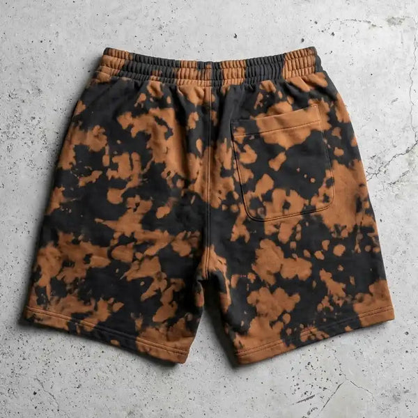 Back view of Ghostreet black and rust bleach wash sweat shorts laid flat on a concrete surface, highlighting the elastic waistband and a single back right pocket.