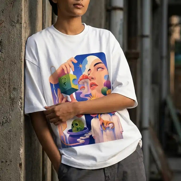 A person leaning against a weathered concrete wall wearing a white oversized graphic T-shirt with a colorful art print and dark gray cargo pants.